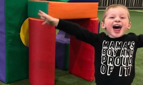 Child smiling with arms wide in front of structure of blocks